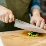Hands slicing cucumber on cutting board, highlighting freshness in food preparation.